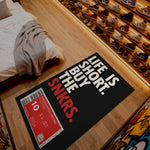 Shoe display with a mat reading 'Life is short, buy the snkrs' on a wooden floor.

