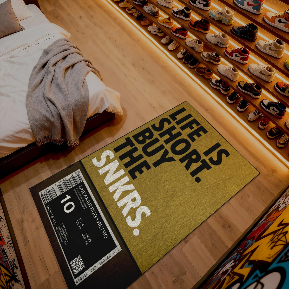 Doormat with 'Life is short, buy the snkrs' text on a wooden floor next to a bed.

