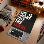 Sneaker-themed rug with 'Life is short, buy the snkrs' text in a bedroom setting.

