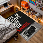 Room with a black rug featuring text and a sneaker-themed design, surrounded by shoes and a bed.


