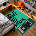 Room with a green rug featuring text and sneaker-themed design, surrounded by shoes and a bed.


