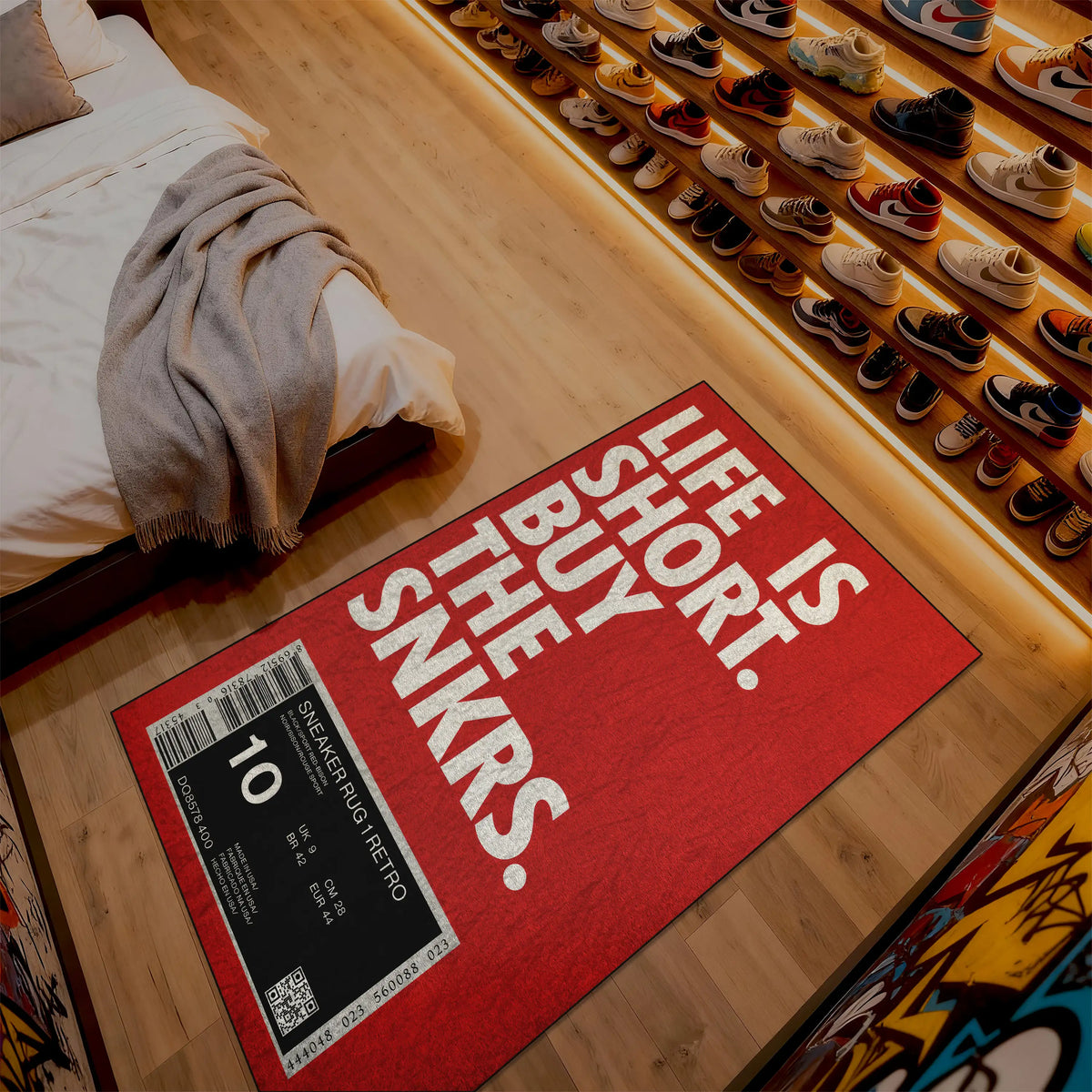 Red mat with 'Life is short, buy the snkrs' text on a wooden floor next to a bed.

